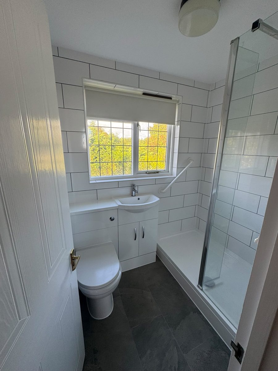 Finished shower room with white metro tiling, slate-effect floor tiles, a vanity unit with a basin, a close-coupled WC and a walk-in shower behind a glass screen