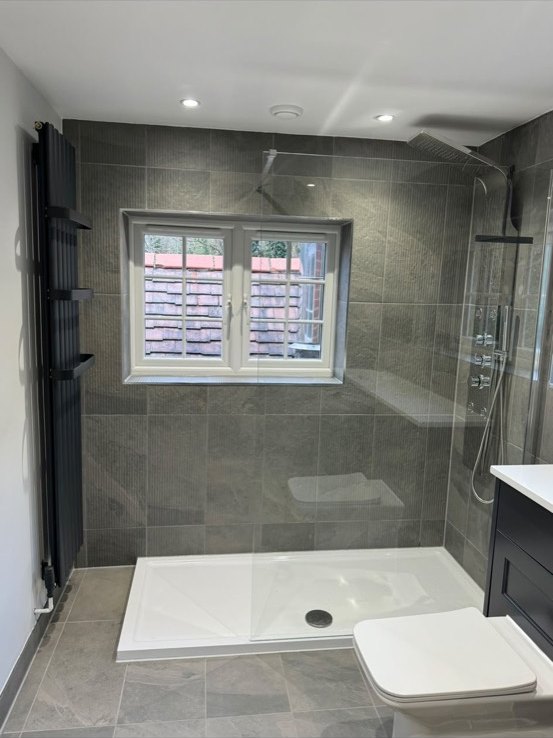 Walk-in shower with grey stone-effect tiles, a chrome shower panel and a black vertical radiator