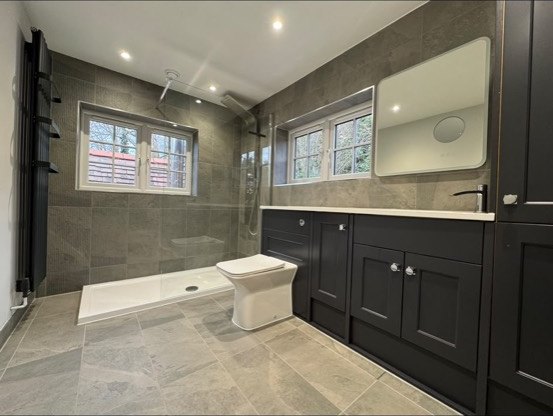 Grey-tiled bathroom with a level-access walk-in shower, white toilet and black vanity units