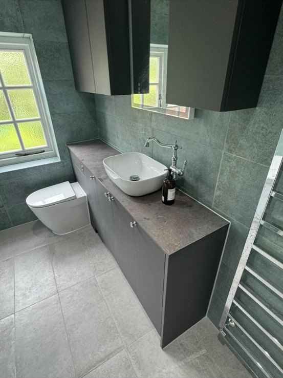 Bathroom vanity with a white counter-top basin, a traditional chrome tap and green-grey stone-effect tiles