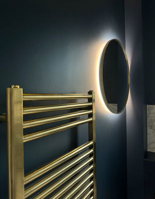 Brushed brass towel radiator and backlit round mirror on a navy wall