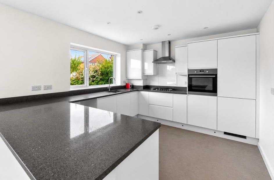 Modern white handleless kitchen with a dark speckled worktop, undermount sink, gas hob, built-in oven and a chimney extractor hood