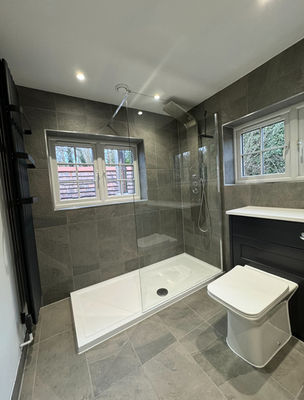 Grey-tiled walk-in shower with a glass screen and two windows