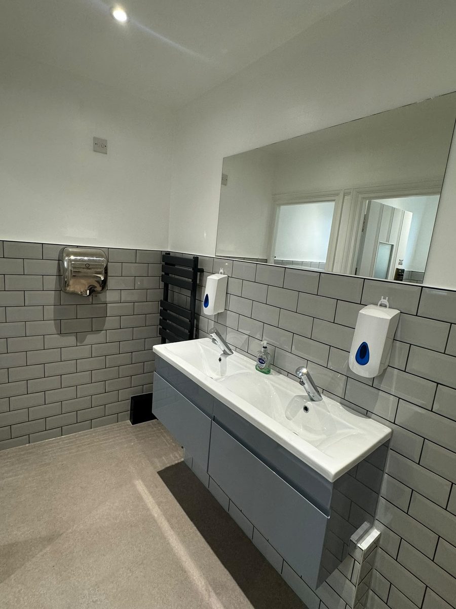 Twin basins set into a grey vanity unit below a large mirror, with a stainless hand dryer and an anthracite towel radiator